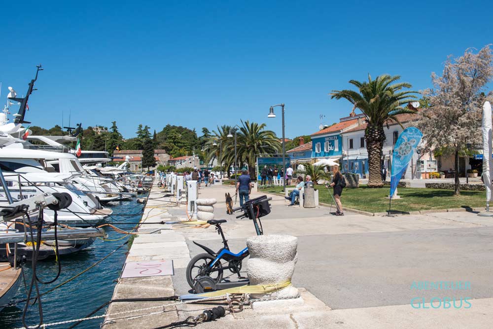 Personen auf der Uferpromenade Riva am Hafen mit ankernden Booten in Vrsar auf der Halbinsel Istrien in Kroatien