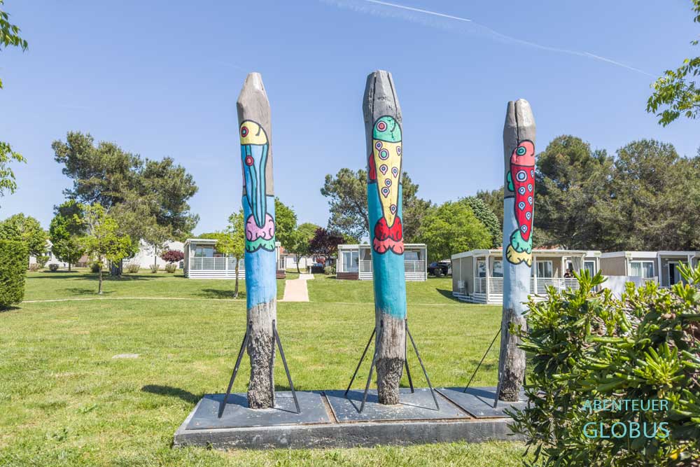 Drei bunt bemalte Holzsäulen und Mobilheime im Hintergrund im Feriendorf Bi Village in Fažana