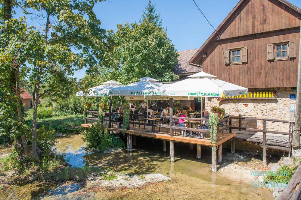 Gäste auf der überdachten Restaurantterrasse des Guesthouse Pod Rastockim Krovom im Wassermühlendorf Rastoke bei Slunj, Kroatien.